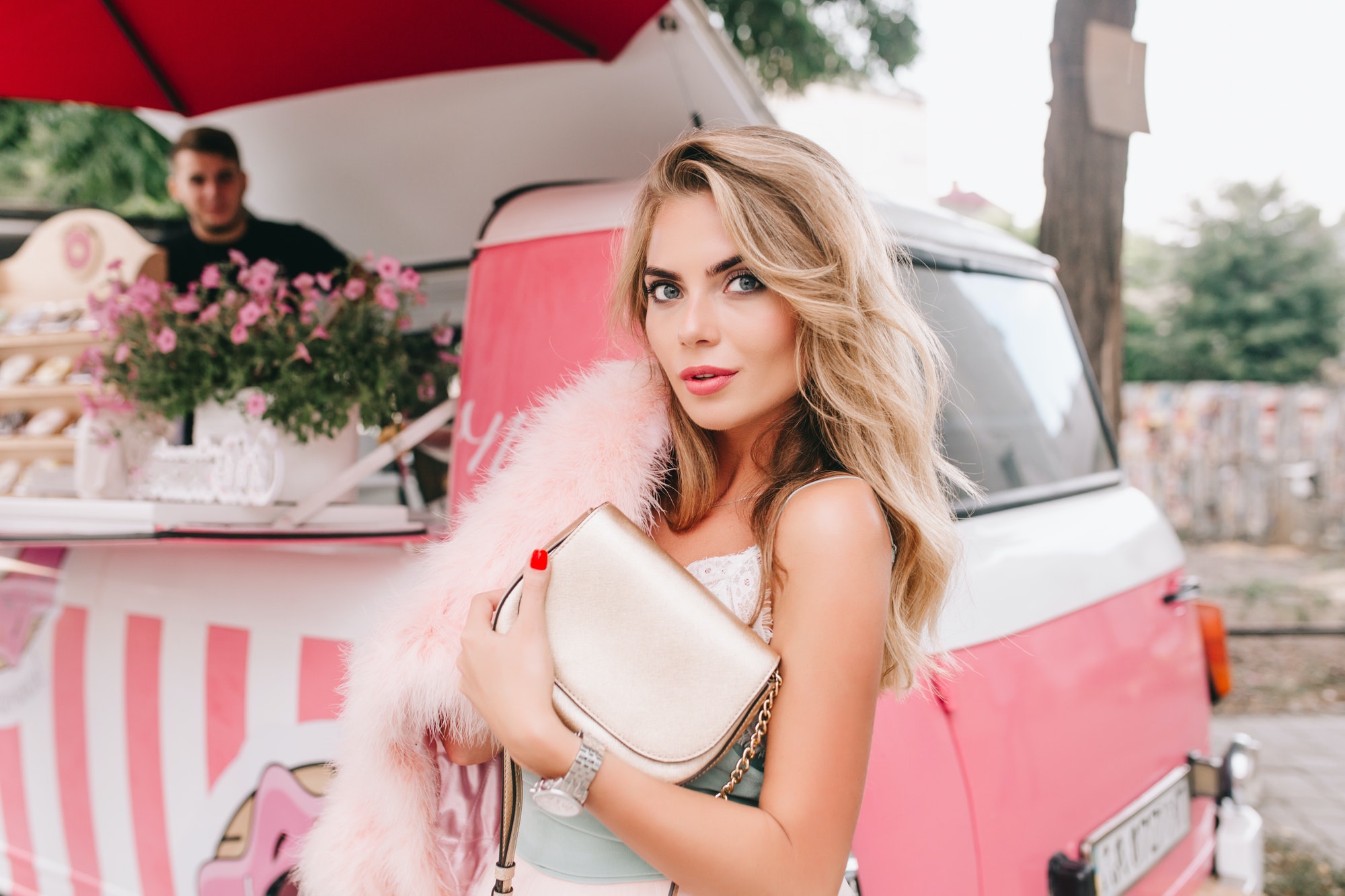 Portrait of fashion model with long blonde hair on retro coffee car background. She holds pink fur s