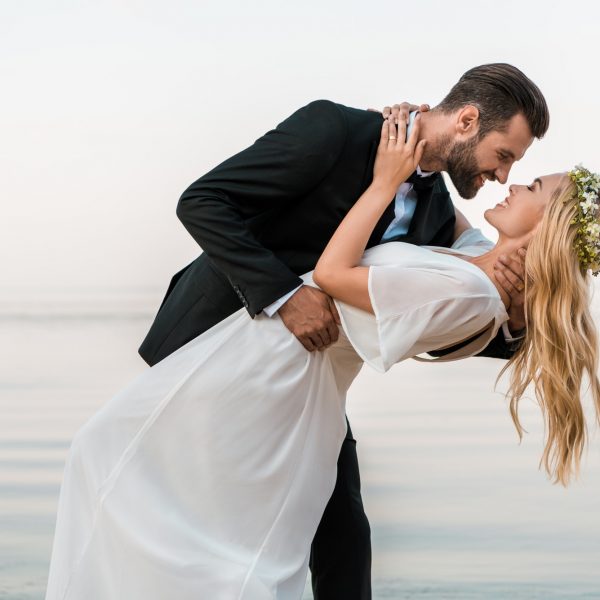 affectionate wedding couple going to kiss on beach